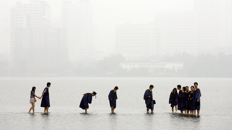 Students in graduation robes stand on a stone bridge submerged underwater at the flooded Donghu Lake in Wuhan, Hubei province, June 21, 2011